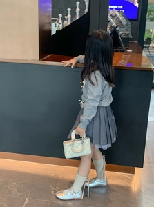 Rear view of child wearing grey knit sweater with white quilted mini bag and pearl handle