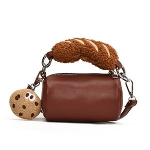 Brown barrel handbag with plush croissant handle and cookie charm on white background