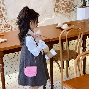 Pink girls bow crossbody bag with gold chain strap shown in a cafe setting