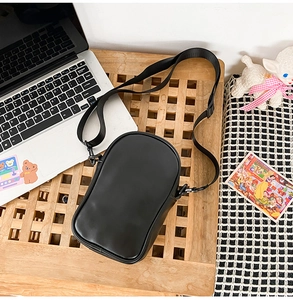 Detailed top view of black laser leather crossbody bag with adjustable nylon strap on wood