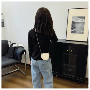 Détail du sac à bandoulière cœur crème avec chaîne en métal sur une jeune fille