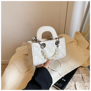 Detail of white quilted crossbody bag featuring large pearl handle and silver metal chain