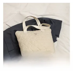 Detail of cream quilted tote bag with heart-shaped stitching and woven handles