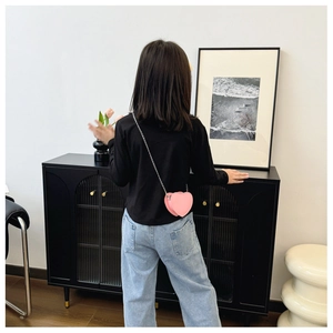 Petit sac bandoulière rose en cuir en forme de cœur avec chaîne porté par un enfant