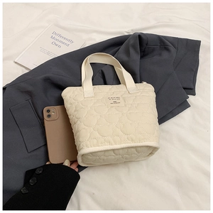 Detail of beige heart-quilted fabric tote bag with soft handles and woven label