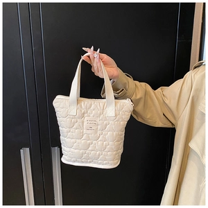 Detail of cream quilted tote bag featuring heart patterns and soft nylon texture