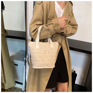 Close-up of beige quilted tote bag showing wave pattern stitching and fabric label detail
