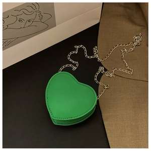 Détail d'un mini sac à bandoulière vert en forme de cœur avec chaîne argentée et coutures fines
