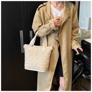 Detail of beige heart-quilted tote bag featuring reinforced webbing handles and zip closure