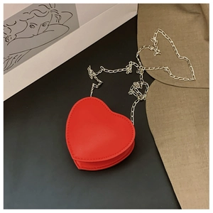 Détail du sac bandoulière rouge en forme de cœur avec chaîne argentée sur un fond sombre chic