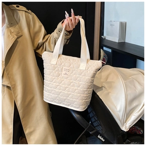 Detail of white heart-quilted tote bag with reinforced handles and brand patch