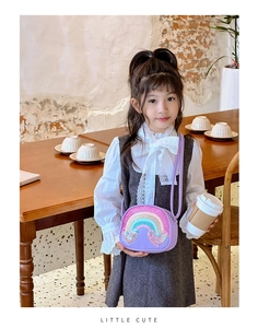 Cute purple rainbow crossbody bag for girls shown with a child model in a cozy cafe setting