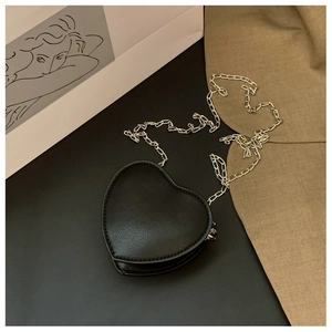 Détail d'un sac cœur en cuir noir avec chaîne argentée élégante sur fond de décor minimaliste