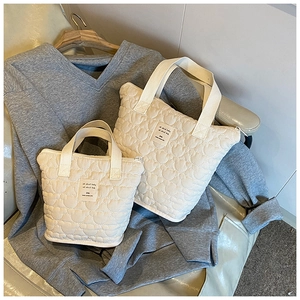 Close-up of off-white quilted tote bags set with wave pattern stitching and fabric labels