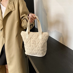Cream quilted tote bag with heart patterns and 'all about baby' tag held by a model