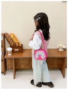 Pink kids crossbody bag featuring rainbow stripes and sequin hearts on a wooden table