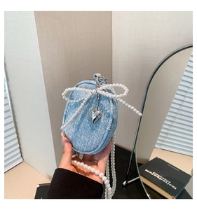 Détail du porte-monnaie en denim bleu avec nœud en perles et pendentif cœur en métal