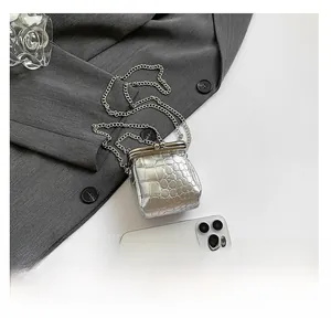 Close-up of silver mini chain bag with stone texture and metallic finish next to a phone