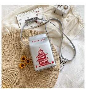 Detail of creative silver takeout box shaped crossbody bag with red tower print on straw mat
