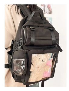 Side view of black nylon ita bag featuring a large clear PVC pocket with a plush bear