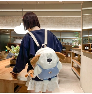 Detail of cute white plush dog backpack with blue overalls and matching small charm
