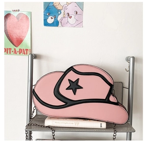 Close-up of pink cowboy hat-shaped crossbody bag with black star detail on metal rack