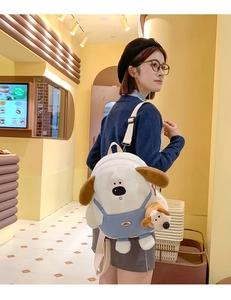 Close-up of cute white puppy plush backpack with blue overalls and a matching mini charm