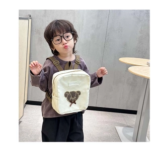 Close-up of cream canvas toddler backpack with a 3D teddy bear patch and green straps