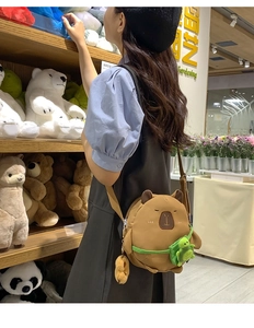 Close-up of cute plush capybara crossbody bag with green turtle backpack on model