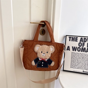 Detail of caramel quilted crossbody bag with a cute 3D bear on a wooden door handle