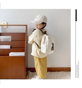 Detail view of white canvas toddler backpack with brown plush bear patch on the side