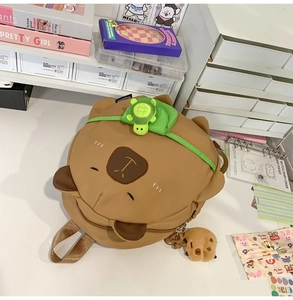 Detail of a brown cartoon capybara backpack with a green plush turtle accessory on top