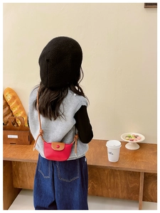 Vue arrière d'un enfant portant un mini sac bandoulière rouge et marron dans un café