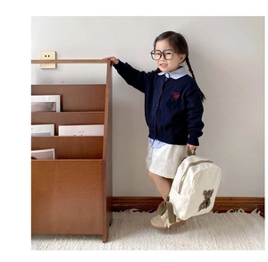 Toddler girl modeling a navy knit cardigan with heart embroidery and a white bear backpack