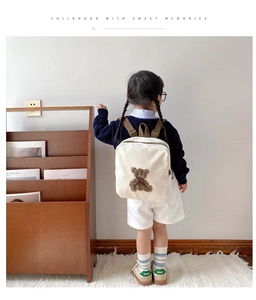 Rear view of a white canvas toddler backpack featuring a bear patch with monogram details