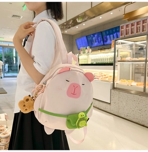 Detailed view of a pink capybara backpack with embroidery and a green turtle pouch charm