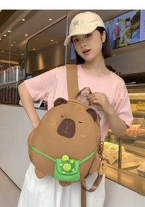 Detail of cute capybara backpack featuring a green pocket and small turtle plush ornament