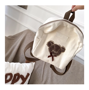 Close-up of cute teddy bear applique and bow on beige canvas toddler backpack