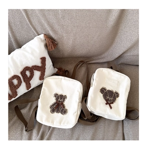 Detail of two white canvas toddler backpacks with cute brown 3D bear embroidery and straps