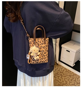 Detail of leopard print crossbody bag with plush charm and adjustable leather strap