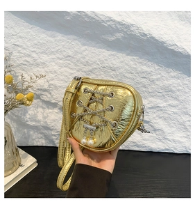 Détail du sac coeur doré avec texture métallisée, lacets en chaîne et perles décoratives