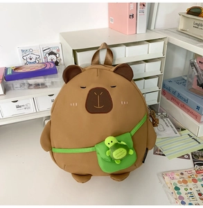 Detail of cute brown capybara plush backpack with green mini bag and turtle keychain