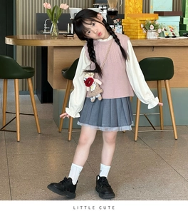 Detailed view of girls' knitted pink vest, white ruffle shirt, and pleated skirt set