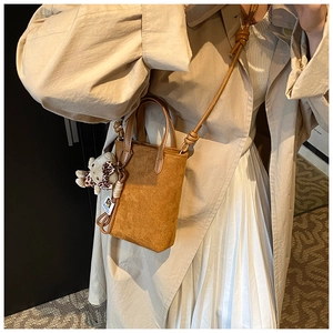 Close-up of brown suede shoulder bag with knot strap detail and bear plush charm