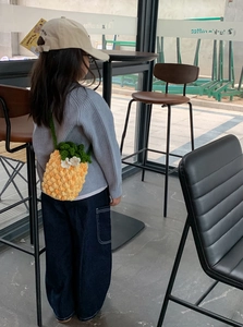 Detailed knit texture of pineapple crochet bag with leaf detail on child model