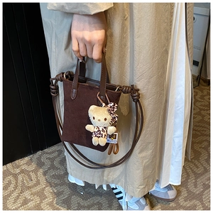 Detail of dark brown suede tote bag featuring a cute leopard-pattern plush bear charm