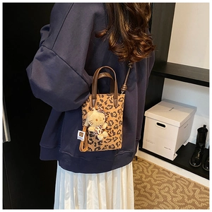 Detail of leopard print mini tote with brown leather handles and plush cat charm