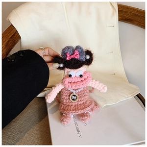 Close-up of pink crochet doll bag with pearl necklace detail on a white hardcover book