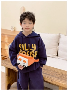 Detalle de un niño con sudadera azul marino y un bolso bandolera naranja con forma de coche