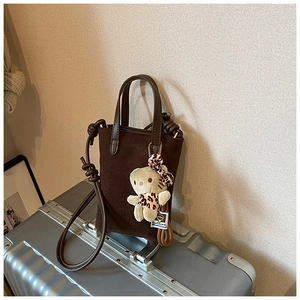Detail of a brown suede mini tote bag with crossbody strap and leopard plush cat charm